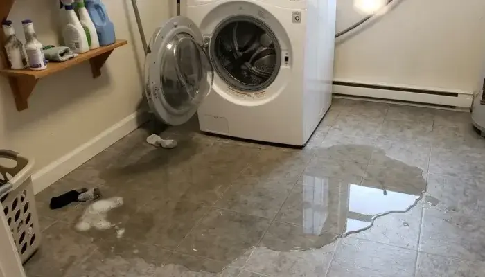 Water pooled across a laundry room floor in front of a washing machine